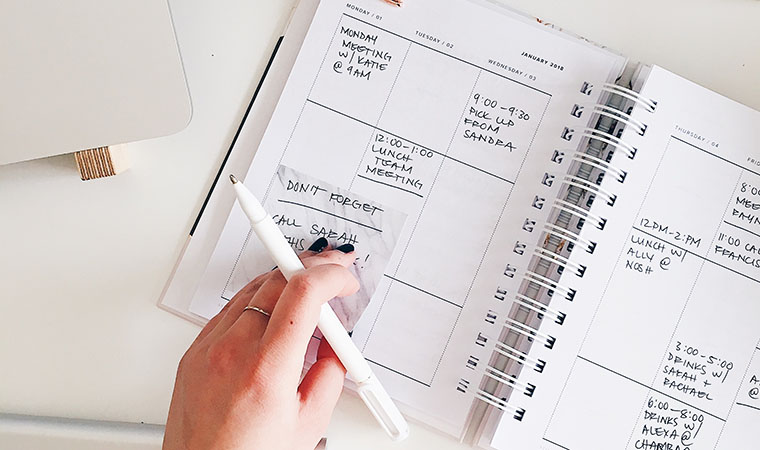 Person adding a sticky note to a day planner.