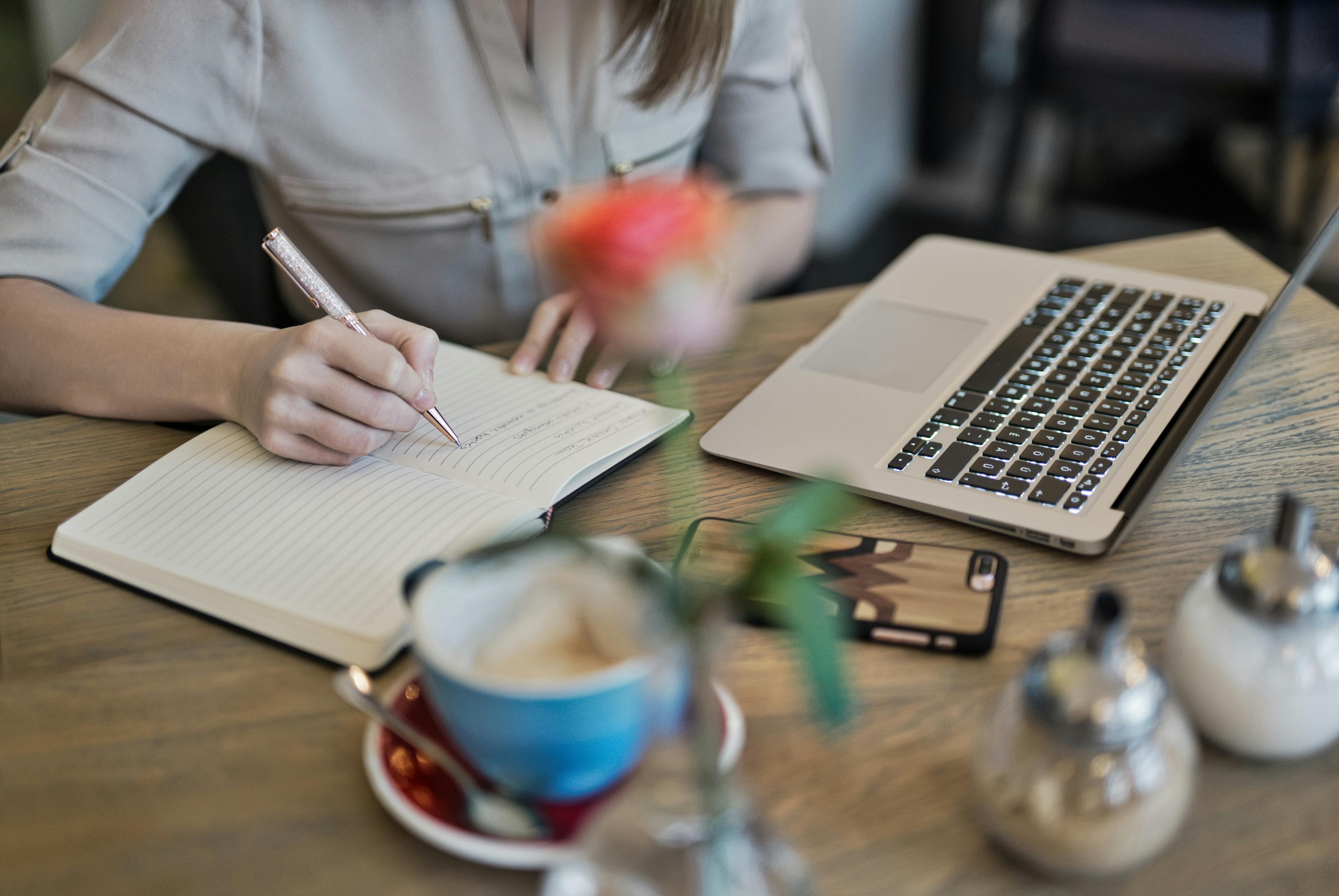 woman writing notes while working on laptop