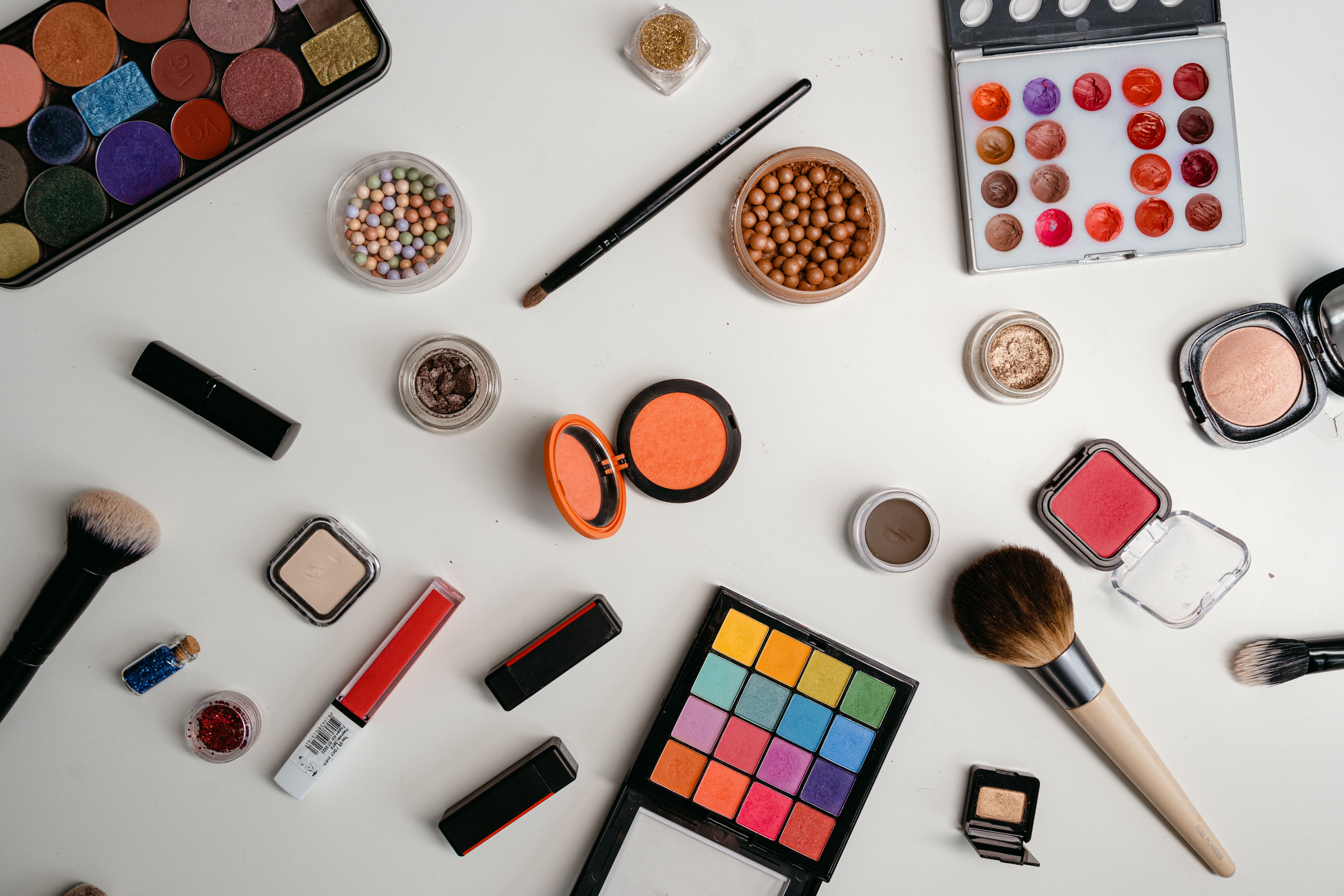 An assortment of beauty products, including makeup brushes and cosmetics, arranged on a white surface, symbolizing personal expression and transformation.