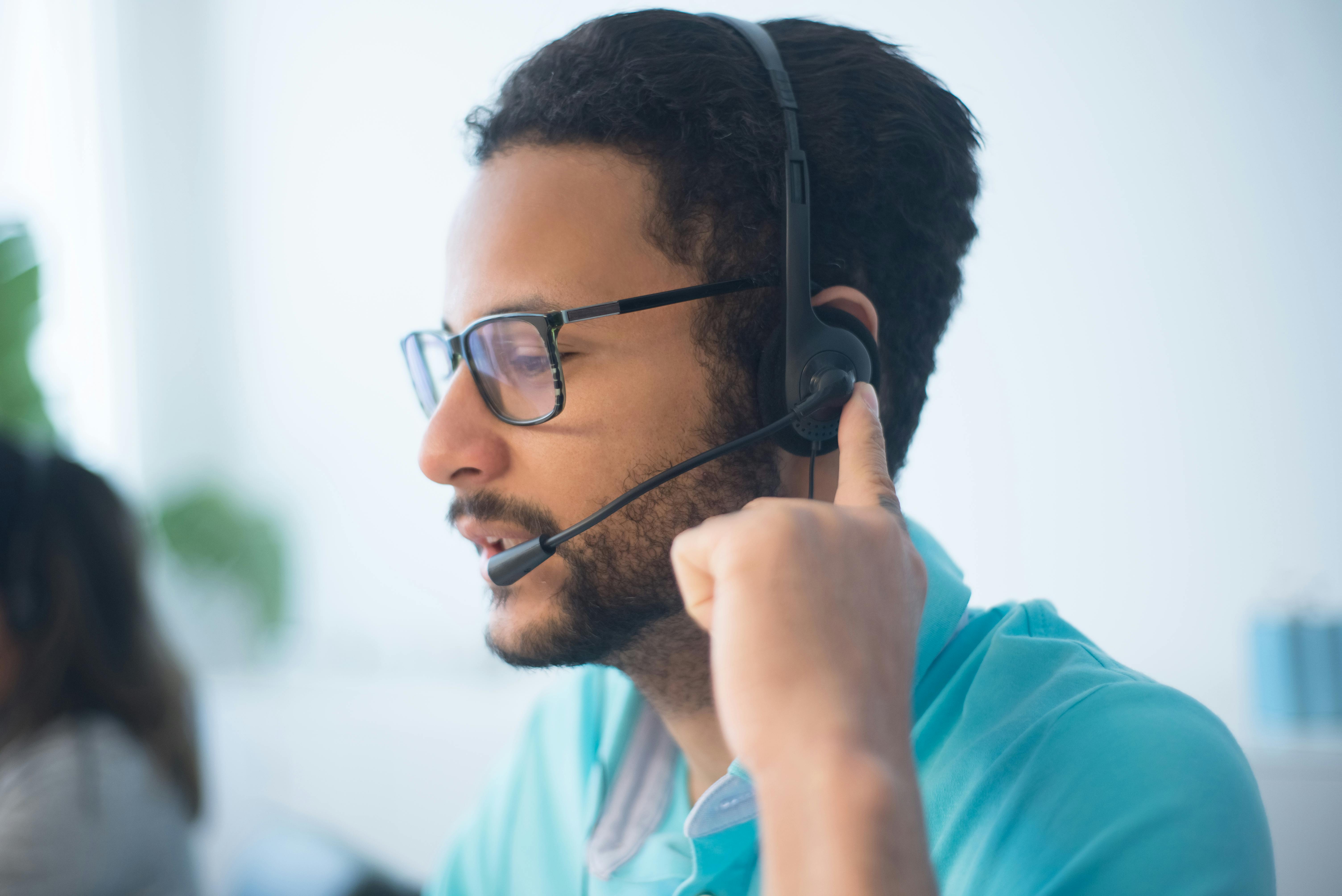 Close-up shot of a man wearing eyeglasses and headphones, representing a contact center agent focused on customer interactions.