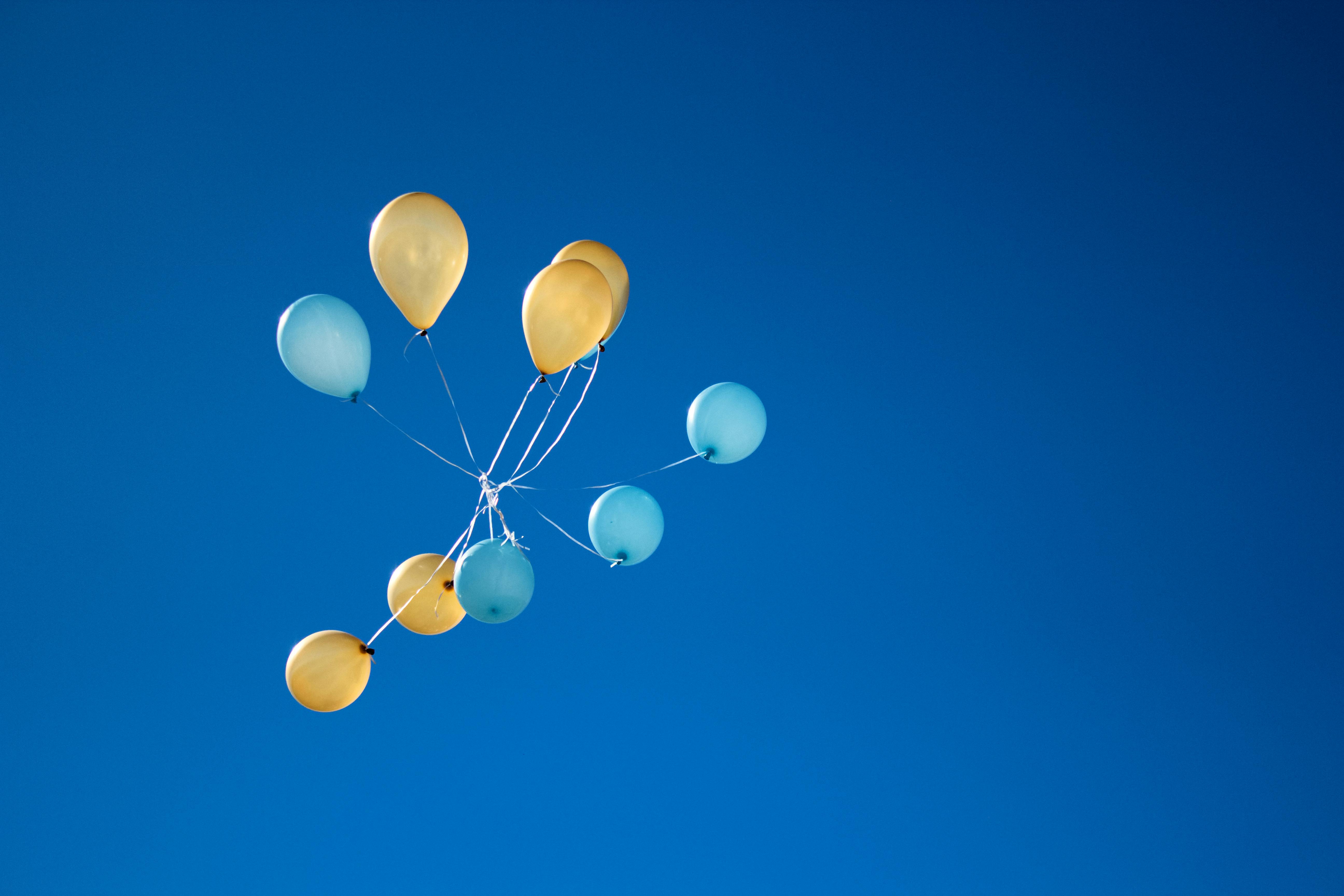 blue and yellow celebration balloons floating up in the sky