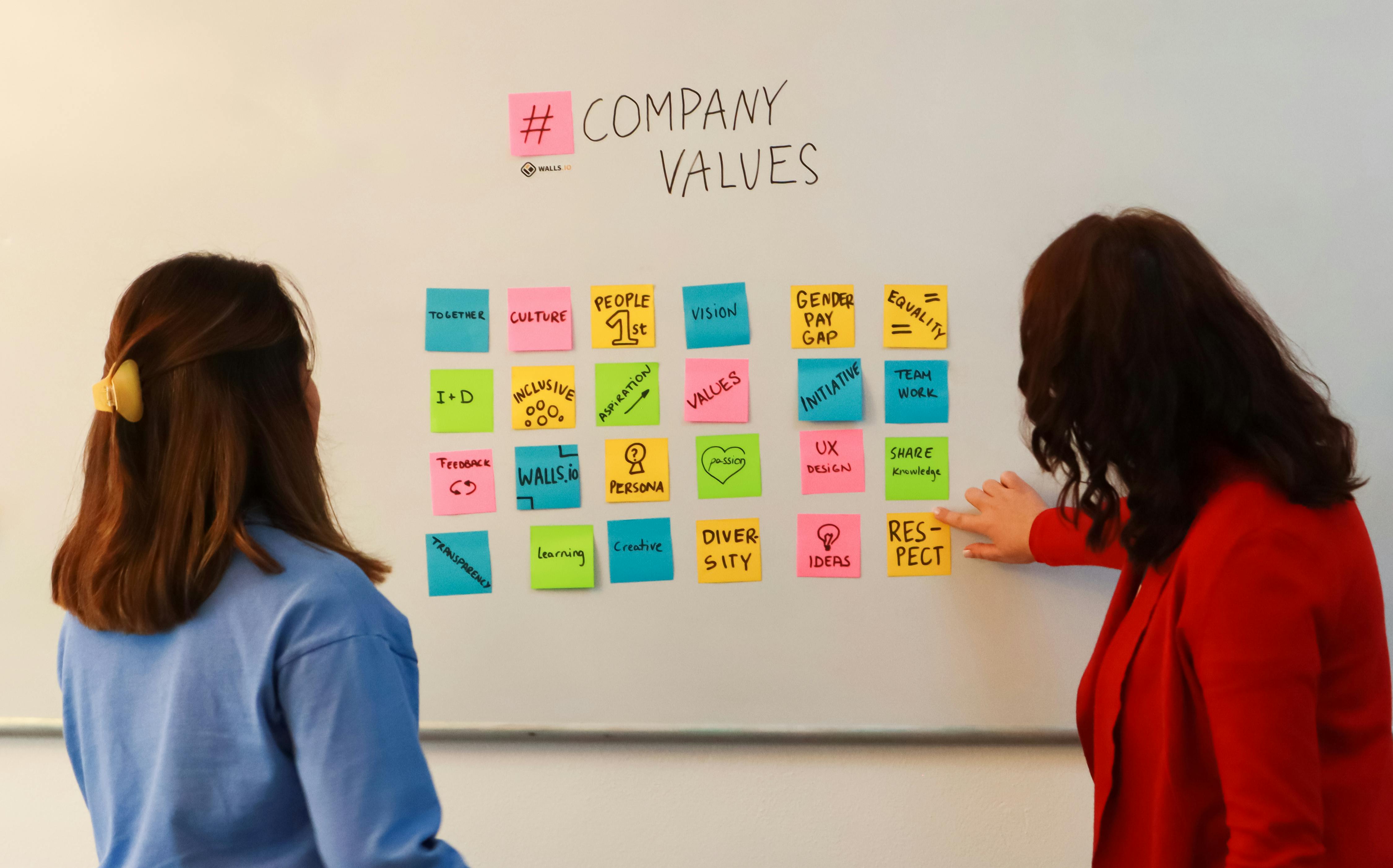 two women working on a whiteboard exercise with sticky notes to determine their company values