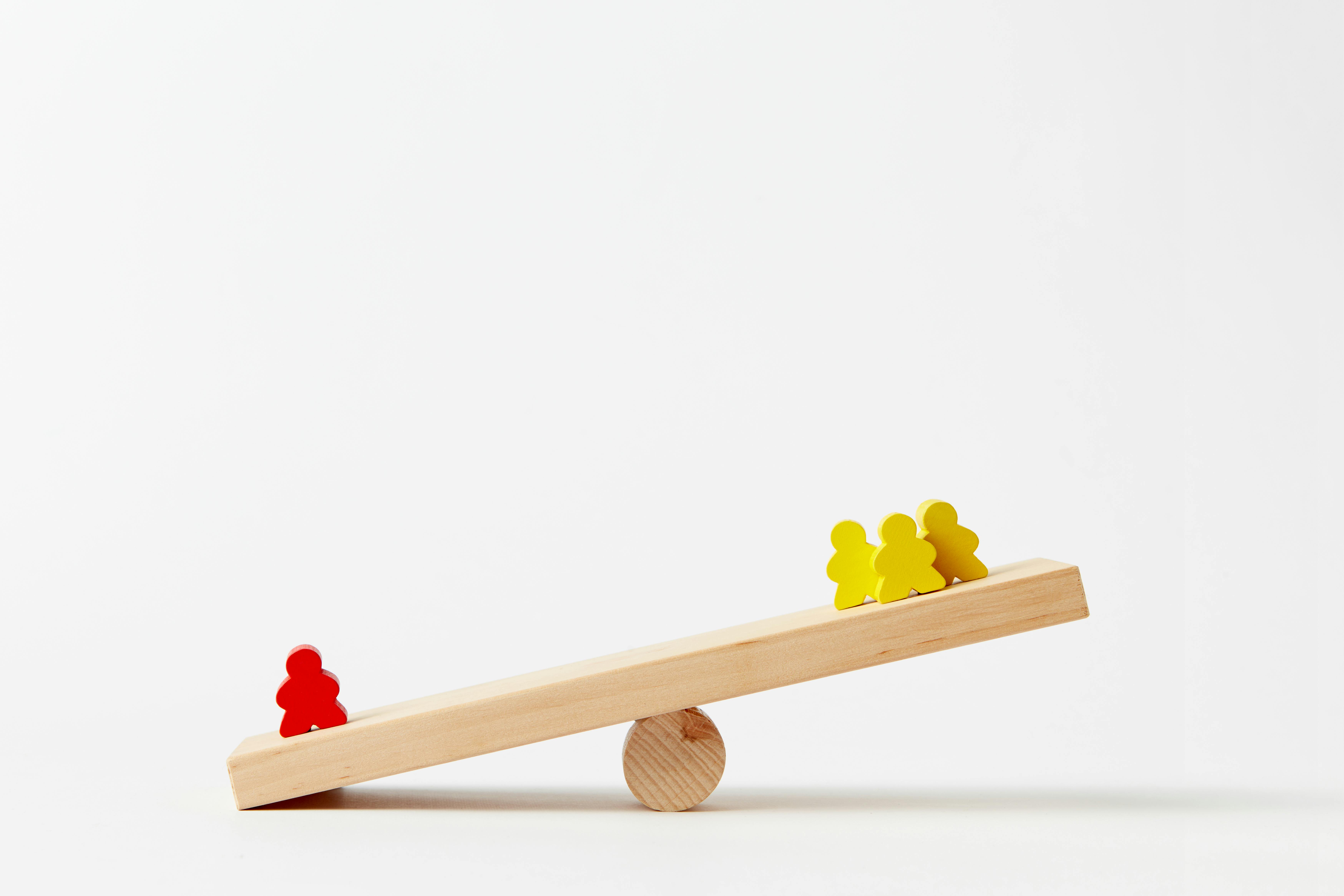 Wooden seesaw balancing human-shaped blocks, symbolizing the balance between employee engagement and product focus in organizational success.