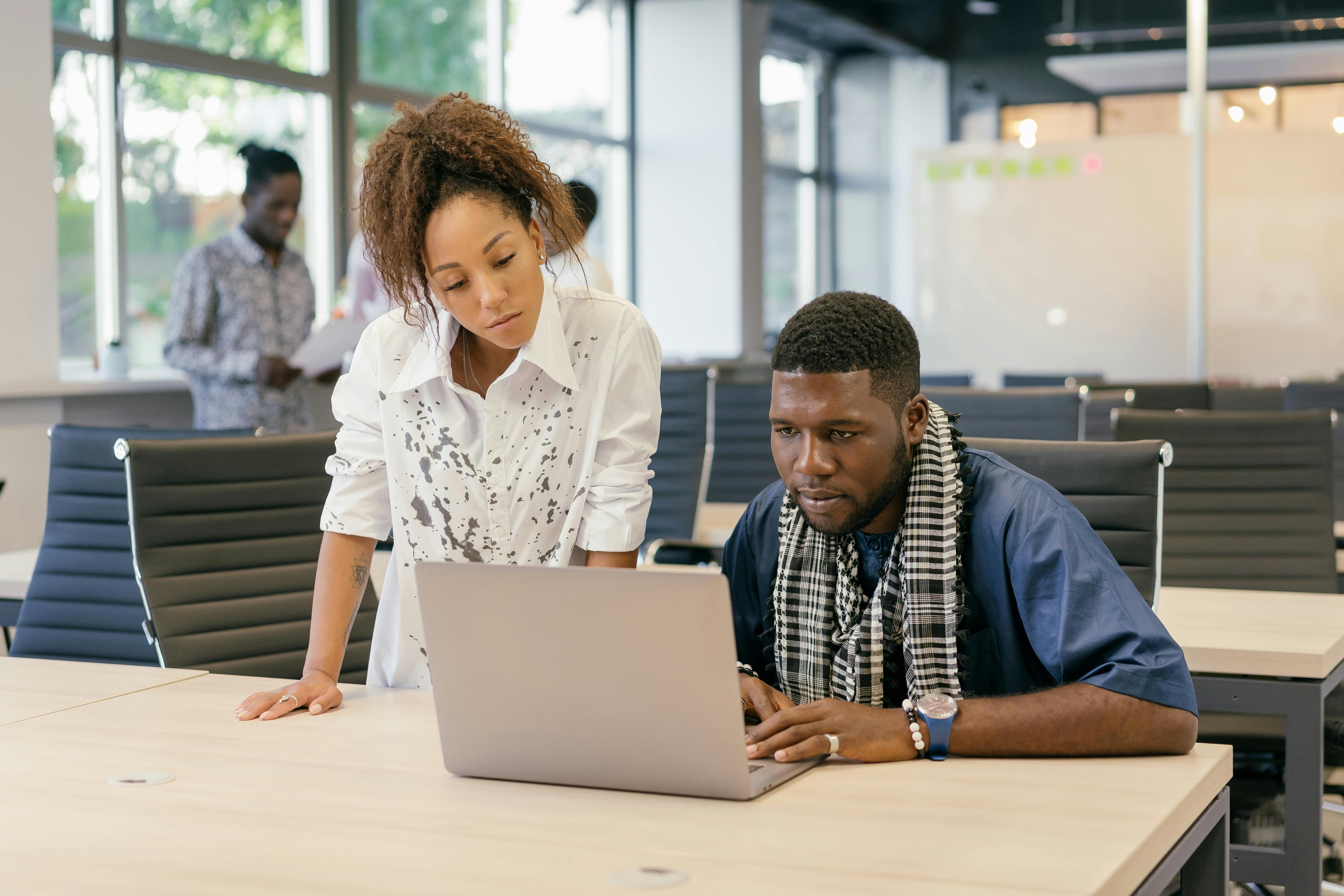 a boss standing alongside her employee reviewing his work on a laptop