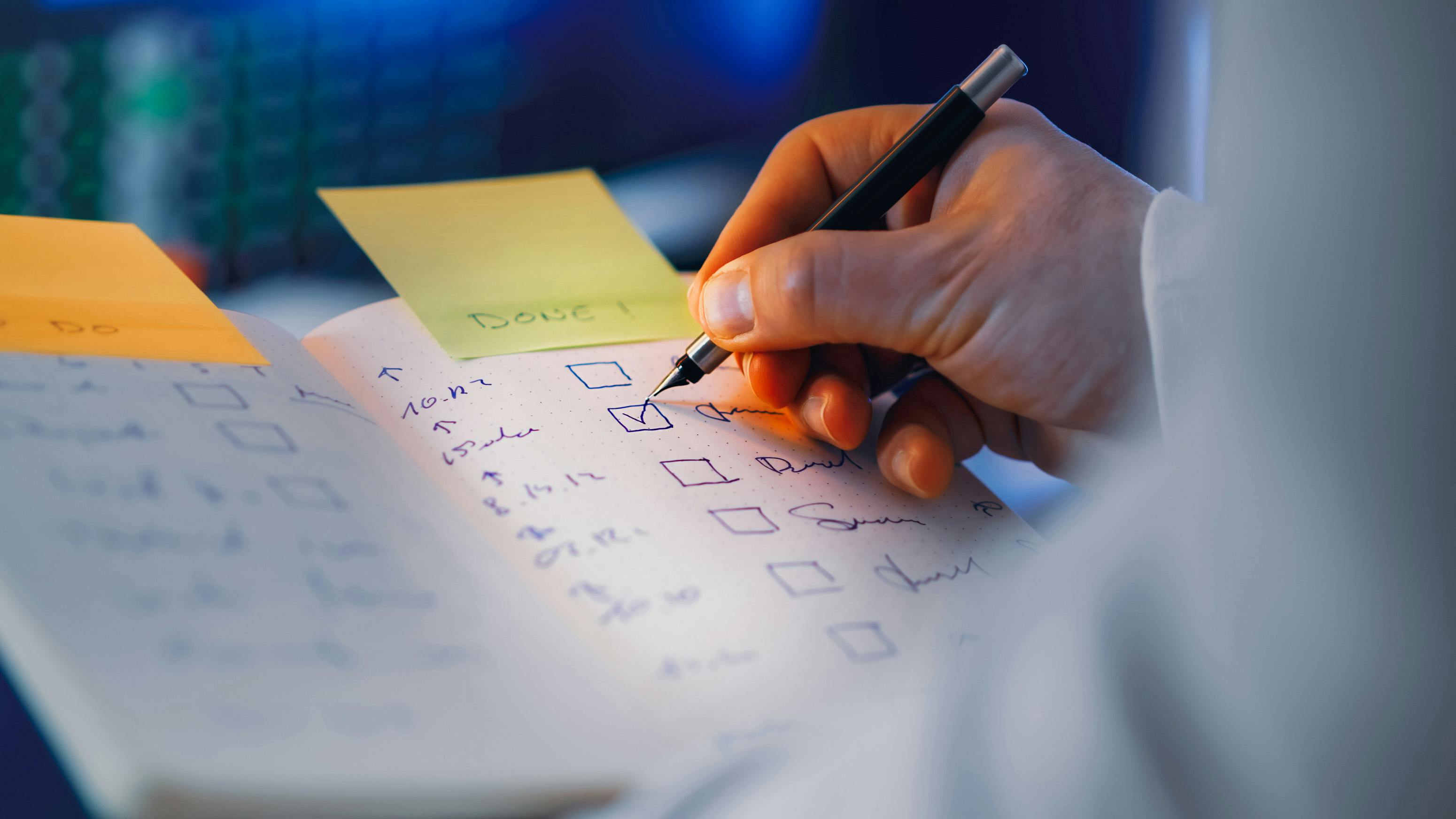 A close-up of a hand writing in a notebook with a checklist prominently in focus, symbolizing task completion and performance tracking.