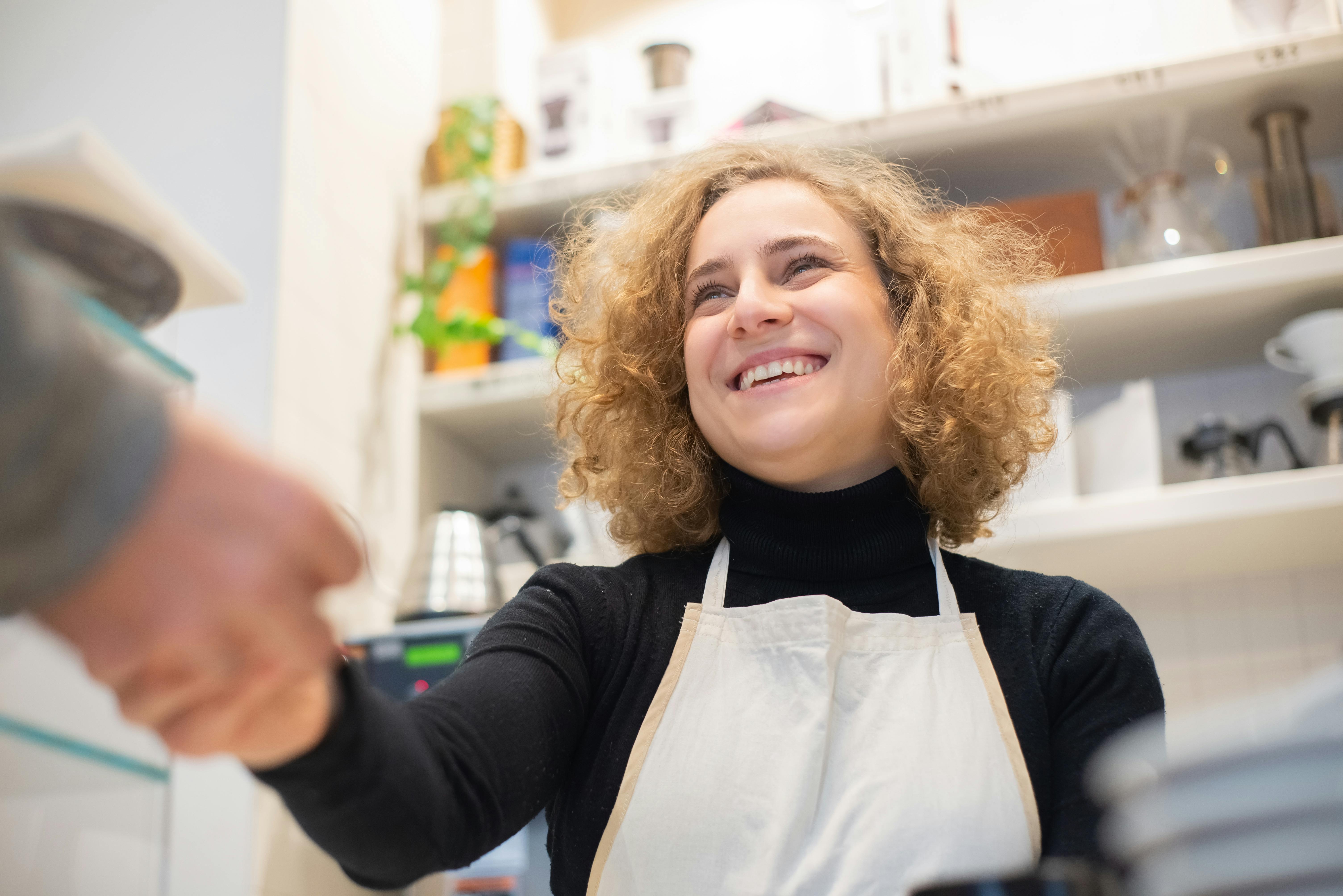 a woman wearing an apron, working in a store and shaking a customer's hand