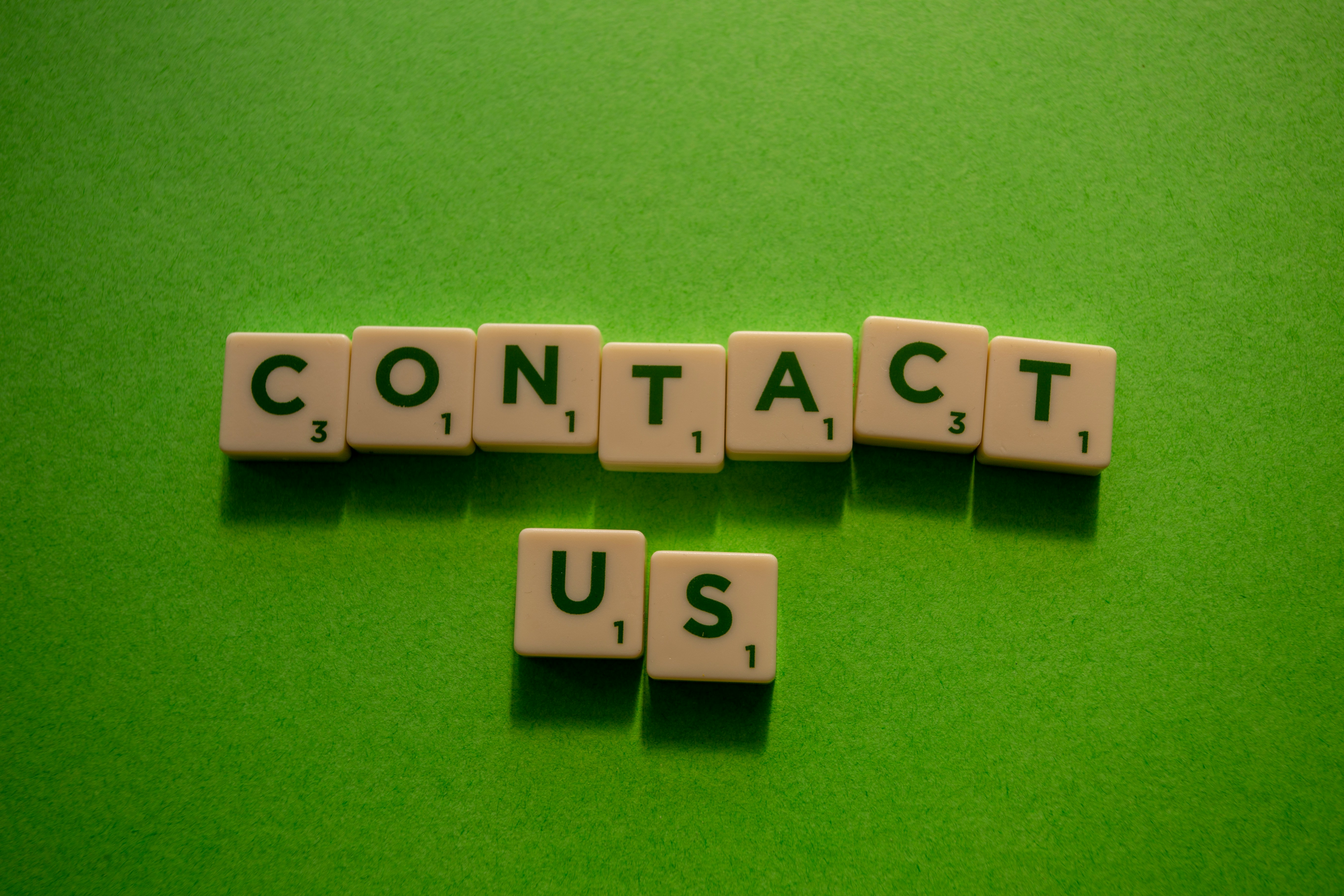 a green background and scrabble tiles that spell out: contact us