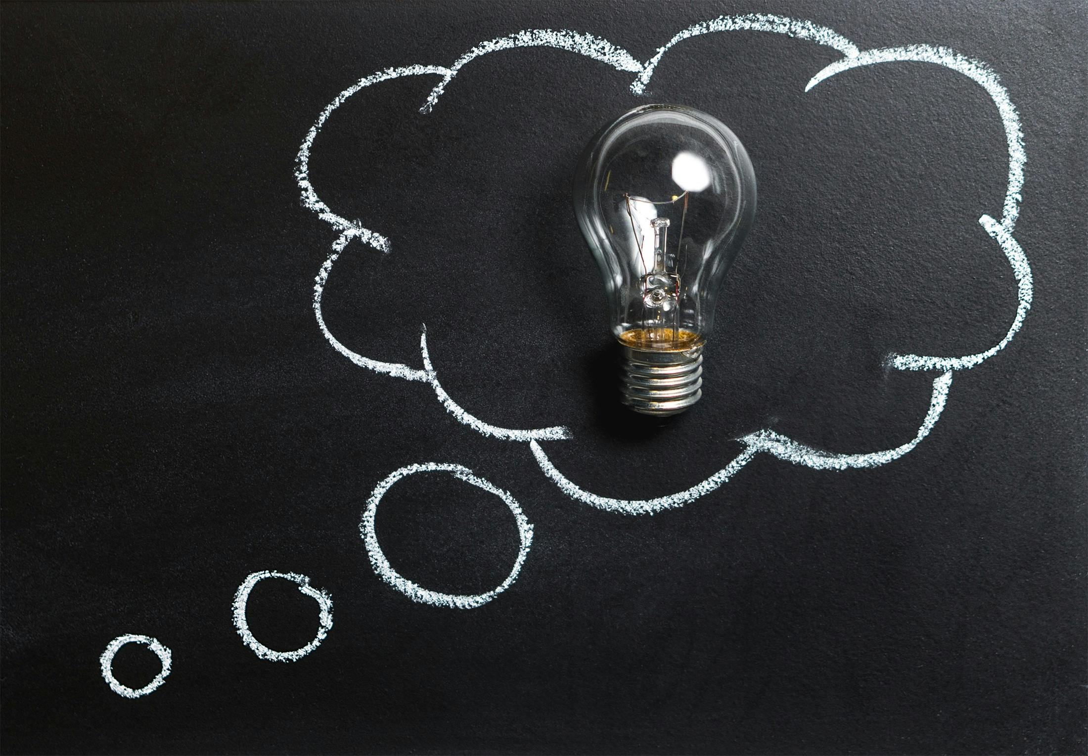 A clear light bulb placed on a chalkboard with drawn lines, symbolizing curiosity, innovation, and the spark of new ideas for process improvement.
