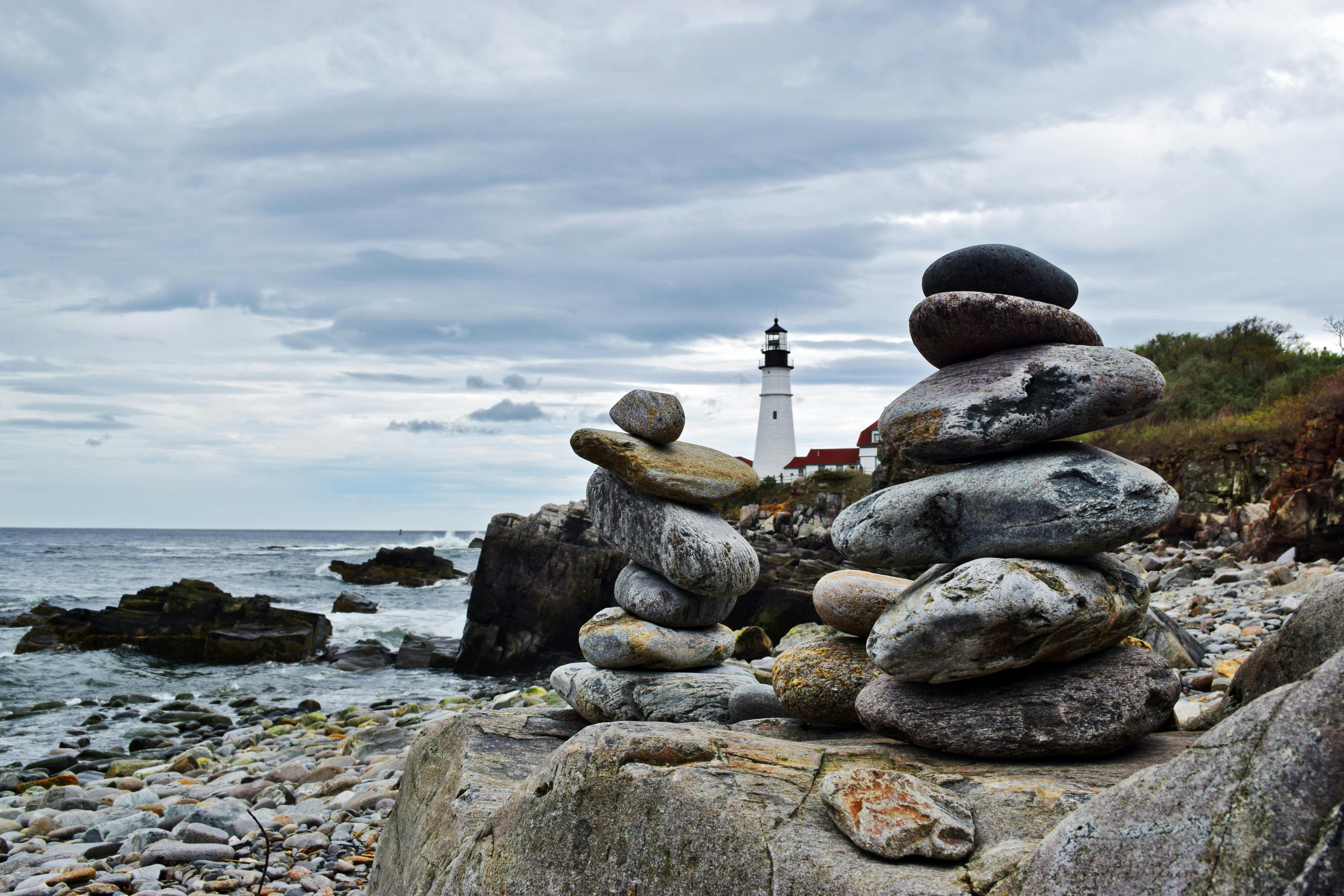 a picture of a lighthouse on a cloudy day on a rocky beach