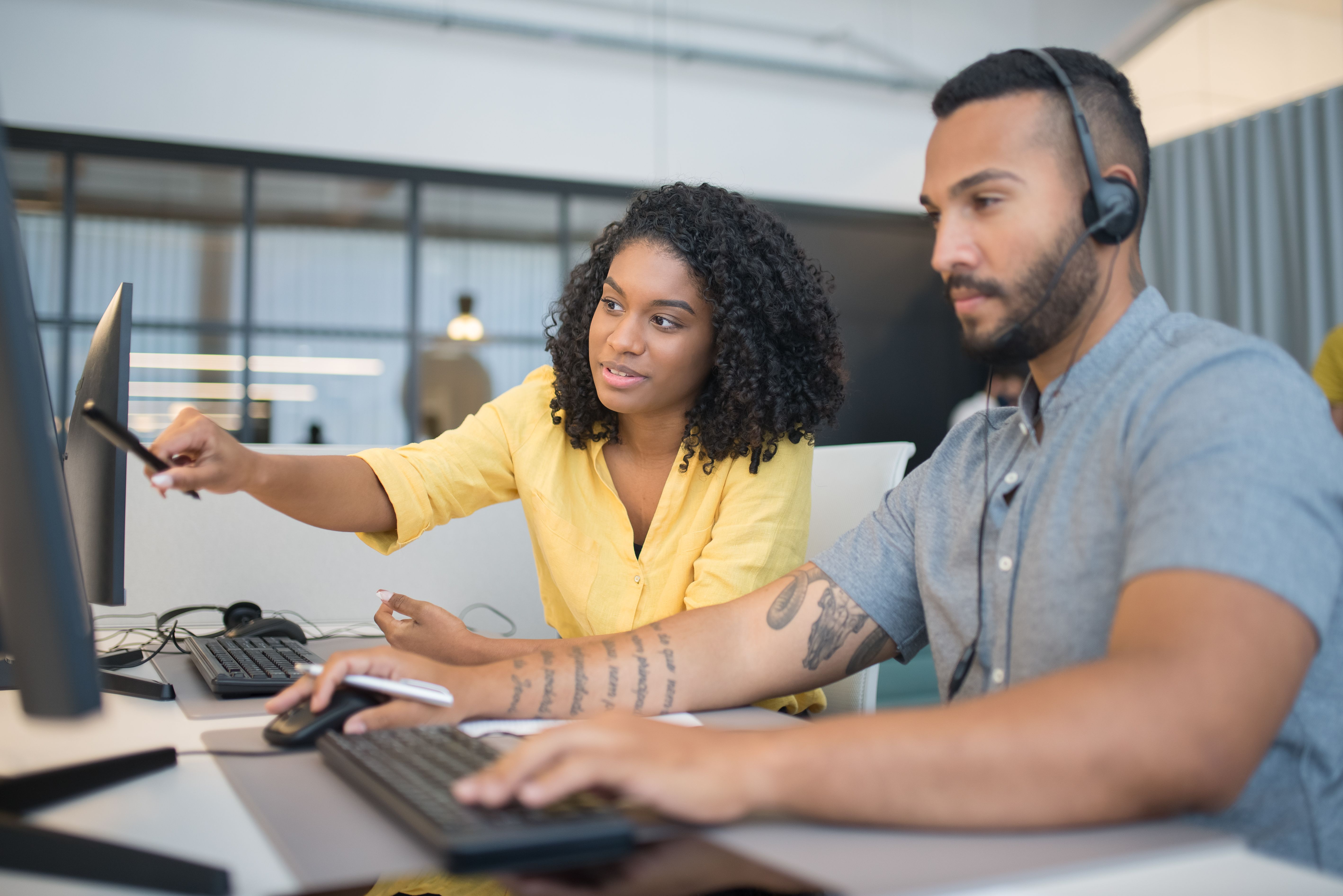 A man and woman working in a call center, wearing headsets and engaging with customers in a professional office environment.