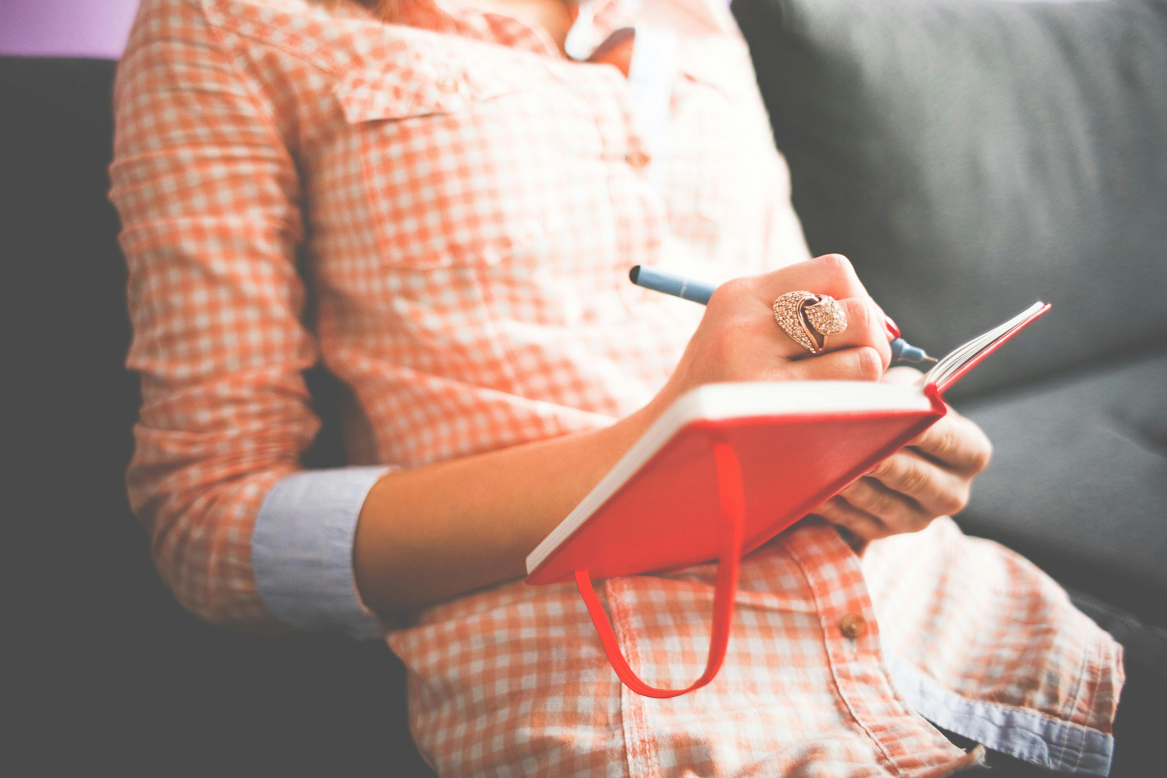 A person writing in a red notebook, symbolizing creativity and personal growth through hobbies.