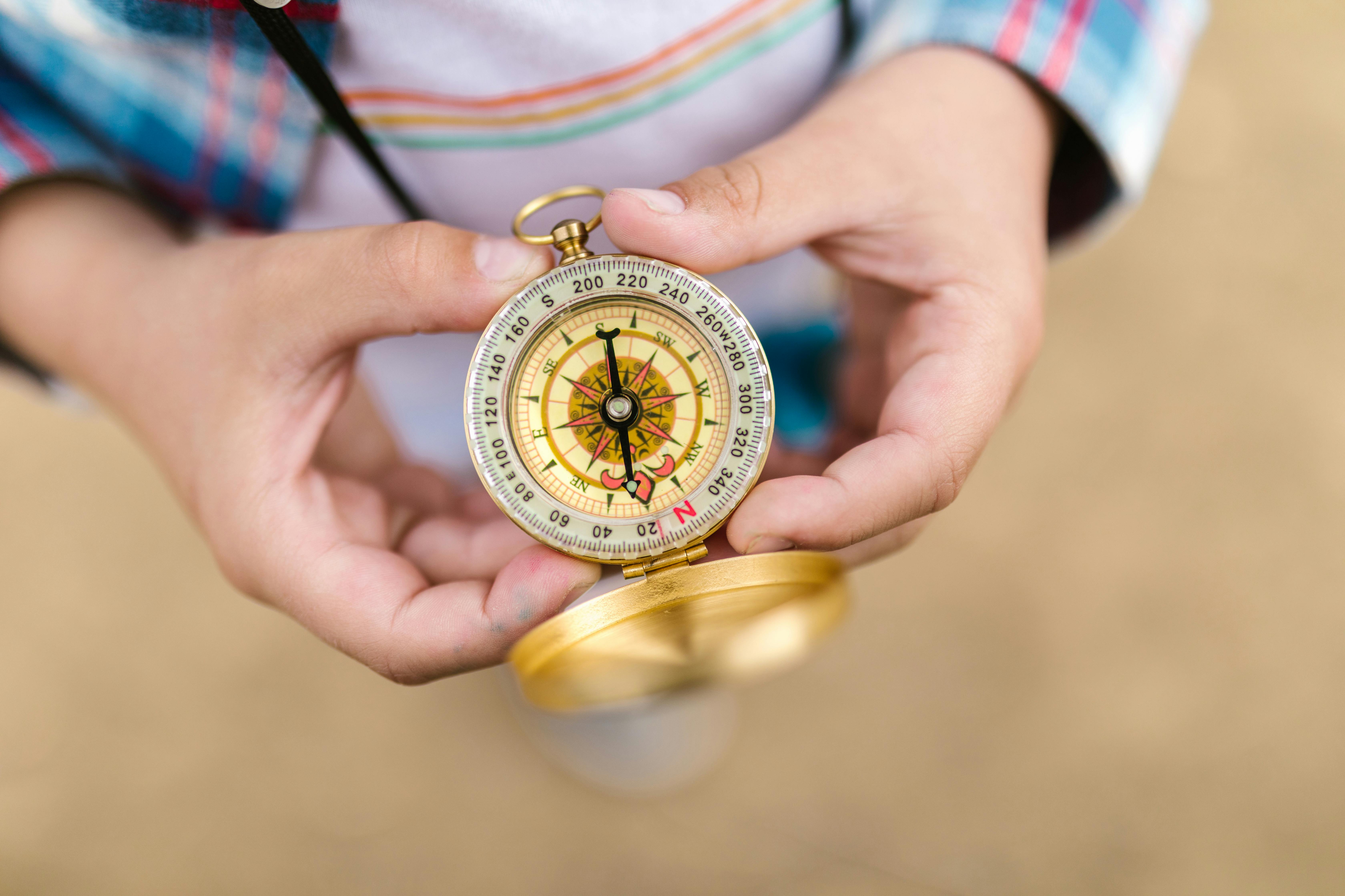 A close-up of a gold and silver compass resting in a person's hand, symbolizing guidance and direction, with a blurred natural background.