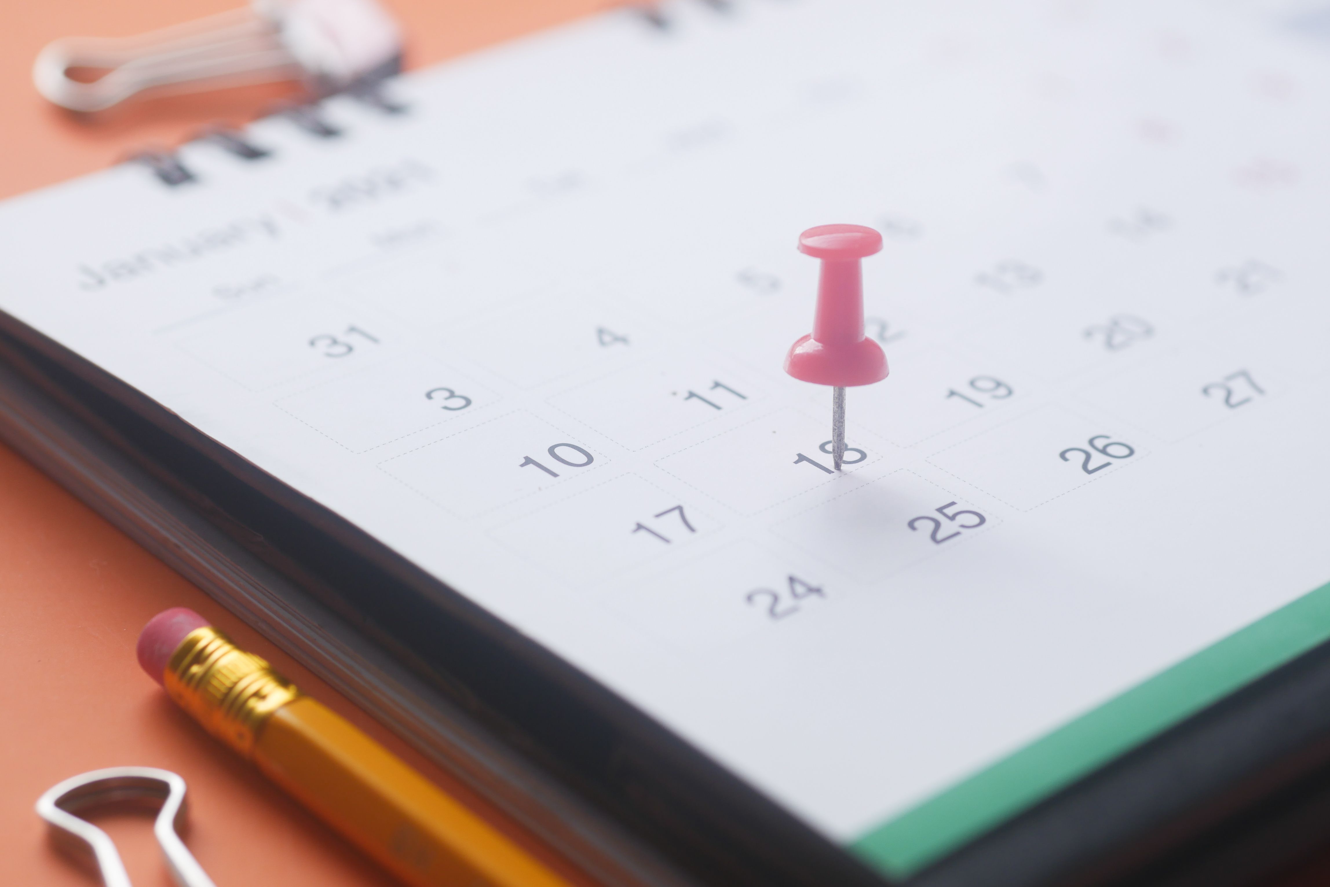 Pink push pin marking a date on a calendar, symbolizing planning and scheduling.
