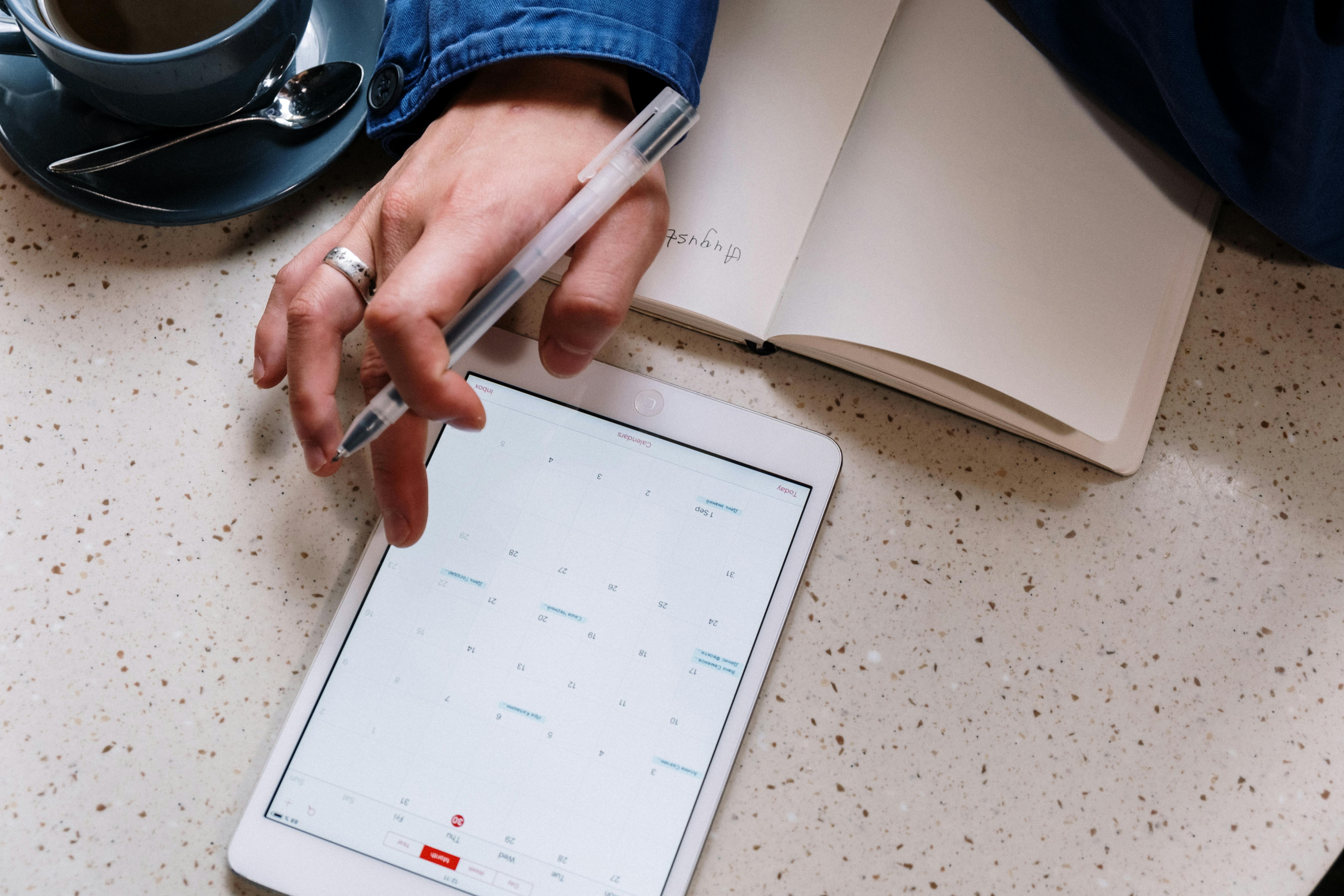 a woman reviewing the calendar on her tablet and writing in a notebook