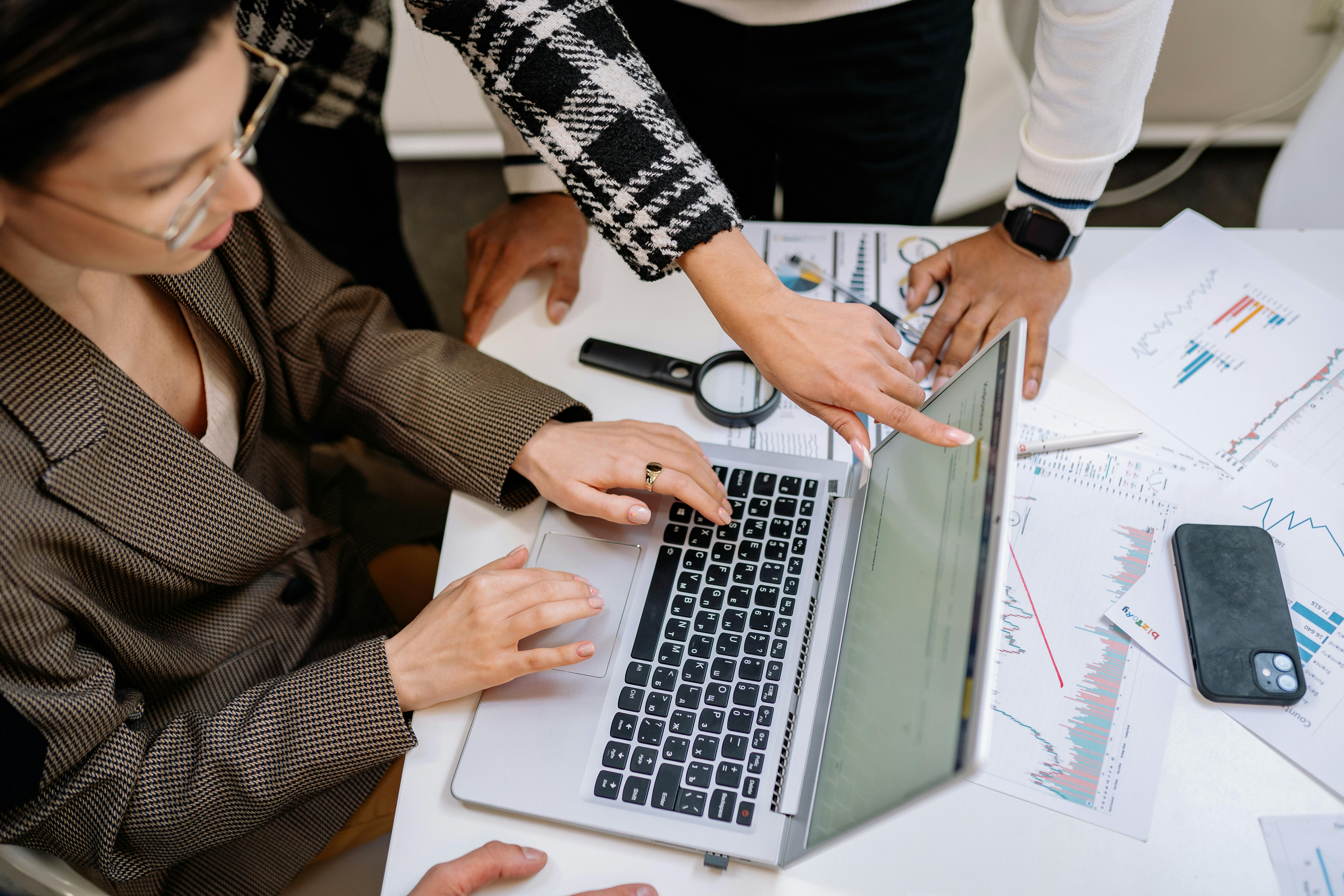 A team of professionals collaborating around a laptop, discussing forecasting strategies and data analysis in a modern office setting.