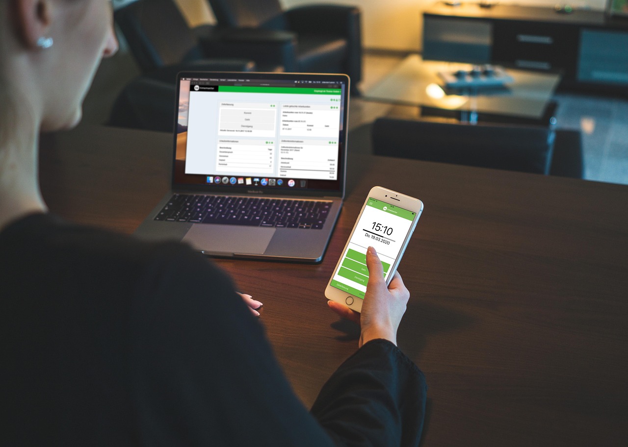 a woman sitting in her office reviewing an attendance report on her laptop and phone