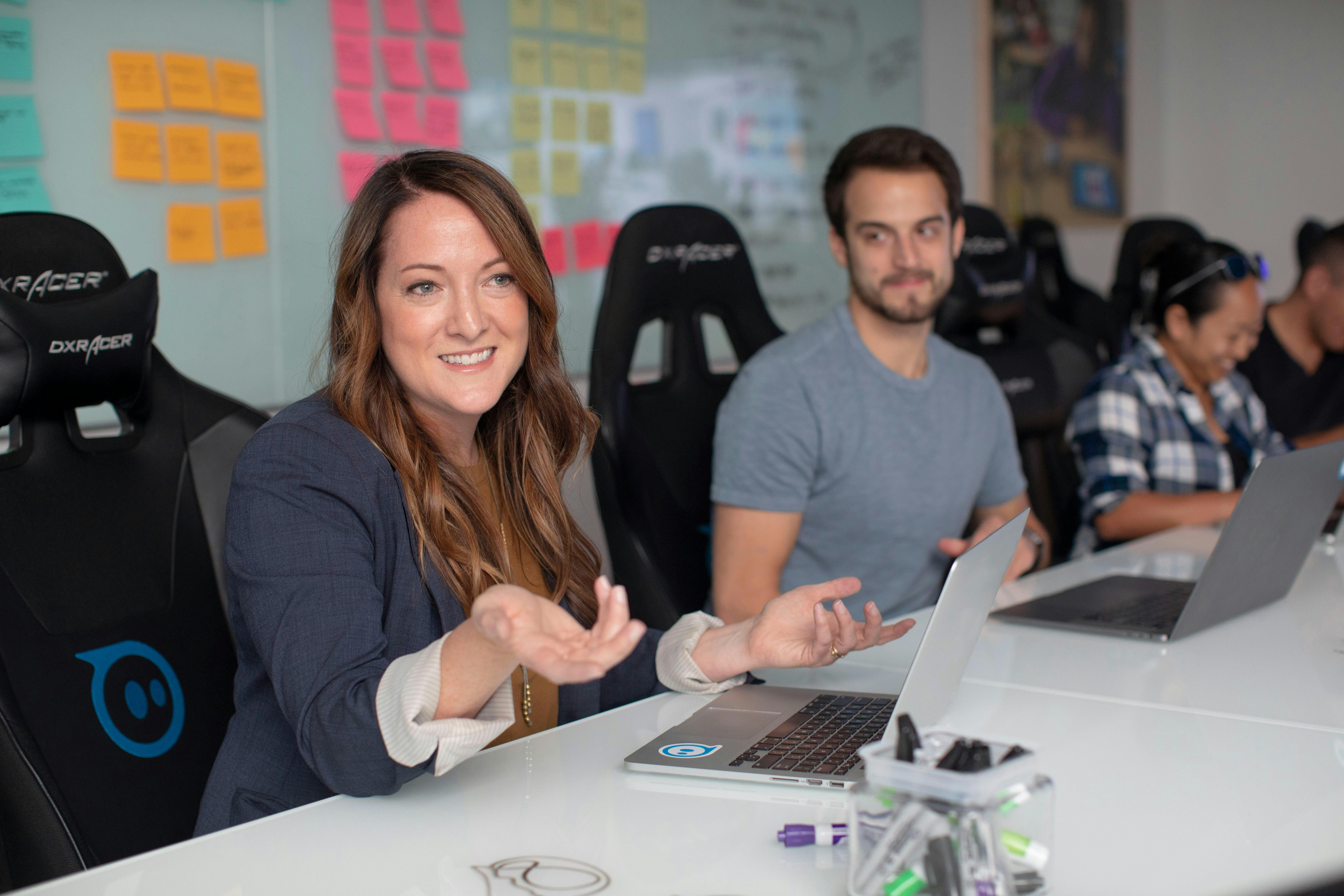 a team sitting in a conference room around a table, while a woman speaks 