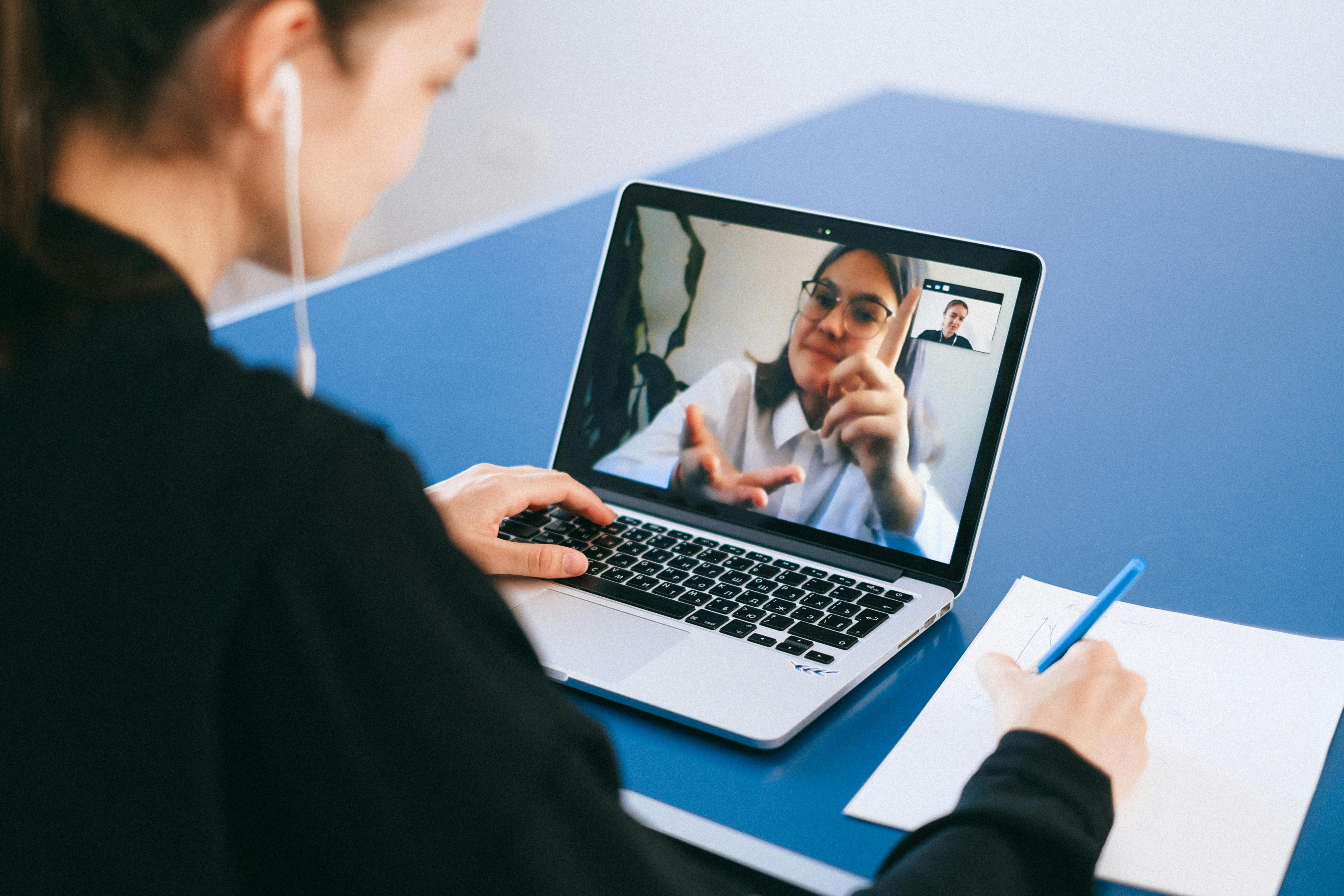 two women meeting virtually on a laptop, one taking notes